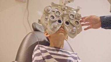 Küçük çocuklar göz muayenesi için göz doktoruna gittiklerinde phoropter kullanmışlar. Doktor elleri phoropter 'i genç çocuğun gözlerine yaklaştırıyor.