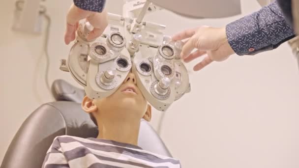 眼科医の眼科医の リトル ボーイズの眼科検査が終わった 医師の手は10代の男の子の目に近いフィルターを置く — ストック動画