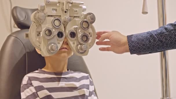 眼科医の眼科医の リトル ボーイズの眼科検査が終わった 医師の手は10代の男の子の目に近いフィルターを置く — ストック動画