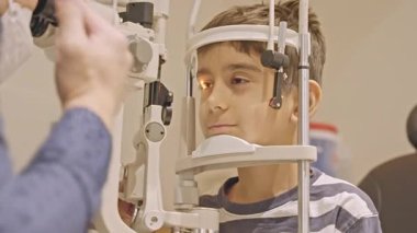 Küçük çocuklar göz muayenesi için göz doktoruna gittiklerinde phoropter kullanmışlar. Doktor elleri phoropter 'i genç çocuğun gözlerine yaklaştırıyor.