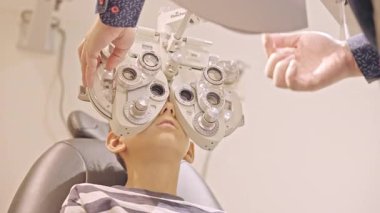 Küçük çocuklar göz muayenesi için göz doktoruna gittiklerinde phoropter kullanmışlar. Doktor elleri phoropter 'i genç çocuğun gözlerine yaklaştırıyor.