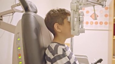 Küçük çocuklar göz muayenesi için göz doktoruna gittiklerinde phoropter kullanmışlar. Doktor elleri phoropter 'i genç çocuğun gözlerine yaklaştırıyor.