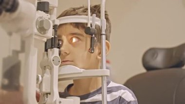 Küçük çocuklar göz muayenesi için göz doktoruna gittiklerinde phoropter kullanmışlar. Doktor elleri phoropter 'i genç çocuğun gözlerine yaklaştırıyor.