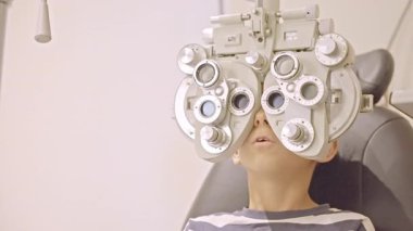 Küçük çocuklar göz muayenesi için göz doktoruna gittiklerinde phoropter kullanmışlar. Doktor elleri phoropter 'i genç çocuğun gözlerine yaklaştırıyor.