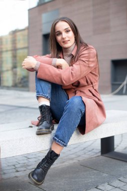 Paltolu, botlu ve kotlu güzel bir manken açık havada bir bankta oturuyor.