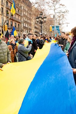 Avrupalılar ve diğer uluslardan temsilciler Ukraynalılar ile birlikte Ukrayna mitingini ulusal sembollerle desteklemek için bir araya geldiler. En büyük Ukrayna bayrağı. Rusya ve Ukrayna arasındaki üç yıllık savaş. İspanya Barselona 23.02.2025
