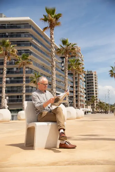 Yaşlı adam parkta günlük haberleri okuyor.