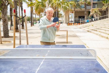 Yaşlı adam dışarıda masa tenisi çalışıyor.