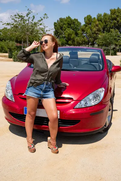 Kırmızı üstü açık arabayla poz veren kadın.