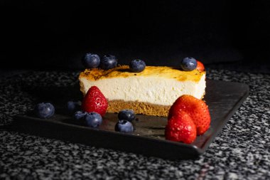 Siyah tabakta çilekli ve yaban mersinli cheesecake, lezzetli tatlı.