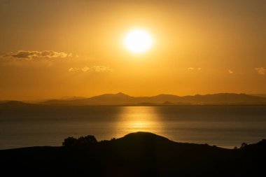 Titicaca Gölü üzerindeki Güneş Adası 'ndan gelen nefes kesici günbatımı Sıcak Altın Tonlar ve Görkemli Dağ Arkaplanı