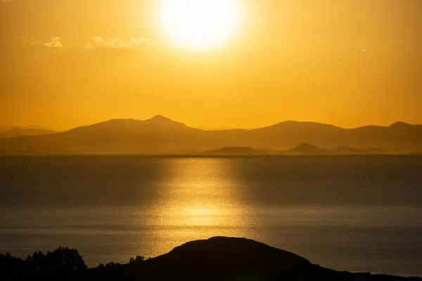 Güneş Adası 'ndan Titicaca Gölü' ne doğru büyülü günbatımı Dağlar ve Parlayan Gökyüzü Yansımaları tarafından çerçevelenmiştir.