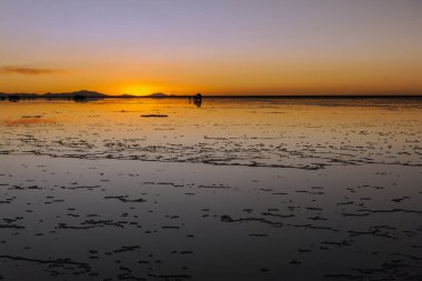 Bolivya 'nın Salar de Uyuni şehrinde dramatik bir günbatımı. Gökyüzünün muazzam düz tuzu, çarpıcı tonlarını yansıtıyor. Çarpıcı ve dünya dışı bir doğa olayı.
