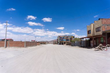 Uyuni Bolivya 'da neredeyse terk edilmiş toprak yol kurak manzaralı basit evler ve yoğun And güneşinin altında ıssız bir atmosfer.