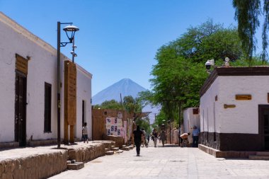 San Pedro de Atacama, Şili. Çöl kasabasında sıradan bir günlük hayat sahnesi, tozlu sokaklarda yürüyen insanlar ve arka planda yükselen bir volkan. Bu And köyü, Kuzey Şili 'de doğal cazibelere açılan popüler bir geçittir.