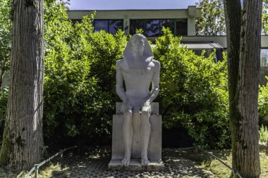 White marble statue of a seated Egyptian pharaoh. The statue is situated in a garden setting, with lush green bushes and trees surrounding it. Maksimir Park Zagreb. clipart