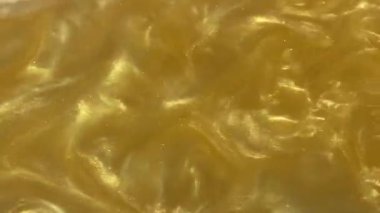 Liquid gold motion organic background. Shine glitter fluid metallic yellow color paint. Texture abstract mica powder cloud swirling underwater.