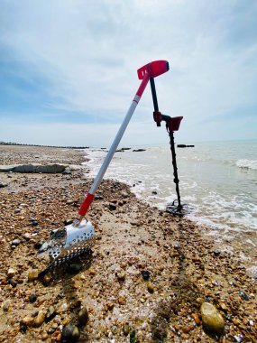 Metal dedektörü ve kumsalda kum kepçesi okyanus kum dalgaları ve arka planda fotokopi alanı olan gökyüzü.