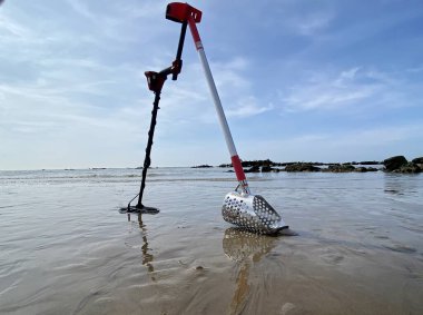 Metal dedektörü ve kumsalda kum kepçesi okyanus kum dalgaları ve arka planda fotokopi alanı olan gökyüzü.