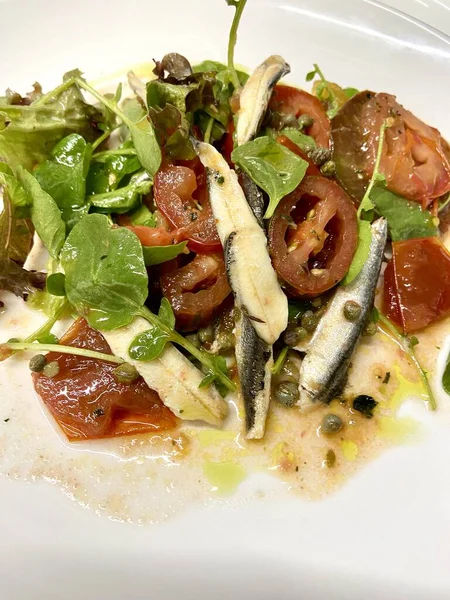 アンチョビ魚サラダと遺産のトマト ホワイトプレートの透かしキャッパー トマトと葉を混ぜたアンチョビ — ストック写真