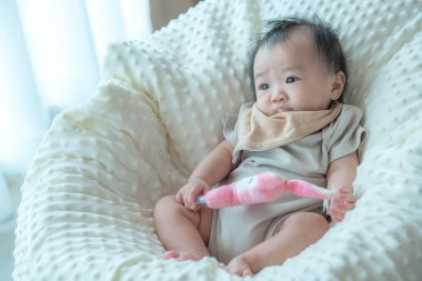 Pembe doldurulmuş bir oyuncakla oynarken yumuşak, rahat bir battaniyenin içinde rahatlatıcı bir görüntü. Bebeğin oyuncakla etkileşime girerken takındığı garip ifade çocukluk ve keşif döneminin güzel bir anını yakalar..