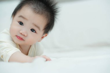 Karnında yumuşak, desenli bir yastığa uzanmış bir bebeğin yakın plan çekimi. Bebeğin şaşı ve meraklı ifadesi, çevreleriyle ilgilenirken çok değerli bir erken gelişim anını yakalar..