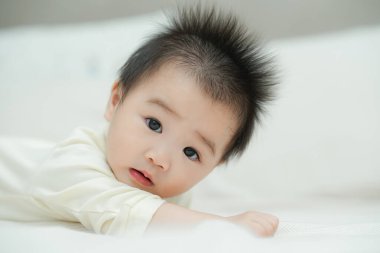 Karnında yumuşak, desenli bir yastığa uzanmış bir bebeğin yakın plan çekimi. Bebeğin şaşı ve meraklı ifadesi, çevreleriyle ilgilenirken çok değerli bir erken gelişim anını yakalar..