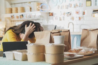 A young woman in a yellow sweater is carefully packing food items into paper bags in a warm, inviting kitchen.Her focused expression and the neatly arranged packaging reflect the dedication and care put into each product. clipart