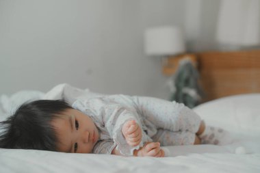 Sevimli bir bebek rahat beyaz bir yatakta uzanır, kollarına yaslanır ve merakla kameraya bakar. Yumuşak yatak örtüsü ve bebeğin masum ifadesi sıcak ve yumuşak bir atmosfer yaratır. Çocukluk zamanlarının tatlılığını yakalar..