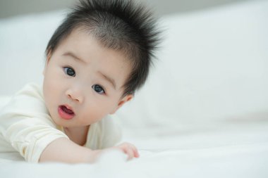 Karnında yumuşak, desenli bir yastığa uzanmış bir bebeğin yakın plan çekimi. Bebeğin şaşı ve meraklı ifadesi, çevreleriyle ilgilenirken çok değerli bir erken gelişim anını yakalar..