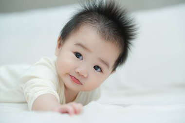 Karnında yumuşak, desenli bir yastığa uzanmış bir bebeğin yakın plan çekimi. Bebeğin şaşı ve meraklı ifadesi, çevreleriyle ilgilenirken çok değerli bir erken gelişim anını yakalar..