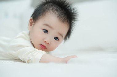 Karnında yumuşak, desenli bir yastığa uzanmış bir bebeğin yakın plan çekimi. Bebeğin şaşı ve meraklı ifadesi, çevreleriyle ilgilenirken çok değerli bir erken gelişim anını yakalar..