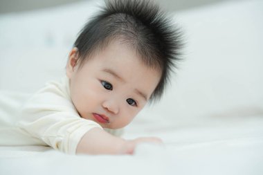 Karnında yumuşak, desenli bir yastığa uzanmış bir bebeğin yakın plan çekimi. Bebeğin şaşı ve meraklı ifadesi, çevreleriyle ilgilenirken çok değerli bir erken gelişim anını yakalar..