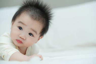 Karnında yumuşak, desenli bir yastığa uzanmış bir bebeğin yakın plan çekimi. Bebeğin şaşı ve meraklı ifadesi, çevreleriyle ilgilenirken çok değerli bir erken gelişim anını yakalar..