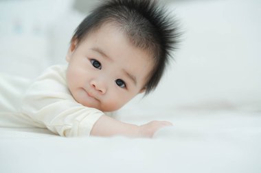 Karnında yumuşak, desenli bir yastığa uzanmış bir bebeğin yakın plan çekimi. Bebeğin şaşı ve meraklı ifadesi, çevreleriyle ilgilenirken çok değerli bir erken gelişim anını yakalar..