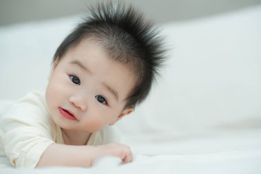 Karnında yumuşak, desenli bir yastığa uzanmış bir bebeğin yakın plan çekimi. Bebeğin şaşı ve meraklı ifadesi, çevreleriyle ilgilenirken çok değerli bir erken gelişim anını yakalar..