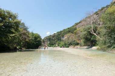 19 Ağustos 2023 - Parga, Yunanistan - Kaplıcalara yakın Acheron nehrinin kanyonunda insanların ılık bir yaz gününde soğuk suyun tadını çıkardıkları inanılmaz doğal manzara. 