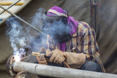 Koruyucu giysiler giyen erkek kaynakçı. Boru hattı dumanını tamir ediyor.