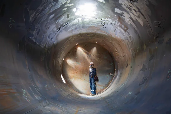 作業男性検査溶接 タンク機器トンネルの地下に閉じ込められた側面の懐中電灯を使用して ストック写真