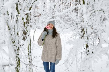 Kışın karlı bir ormanda elinde pembe bir çiçekle gülümseyen güzel bir esmer.