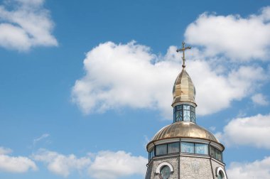 Golden dome with cross atop ornate church tower under blue sky. A spiritual and architectural landmark with religious detailing