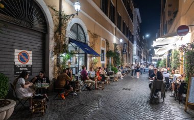 ROME, ITALY - 24 Mayıs 2022: Roma 'da bir yerleşim yeri, insanların geceleri eski bir kaldırım taşı caddesinde küçük bir mahalle restoranında yemek yedikleri yer..