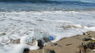 Doğal plaj ekosisteminde deniz dalgaları üzerinde yüzen plastik şişe, çevre kirliliği, yavaş çekim. 4k