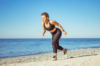 Formda bir kadın güzel bir plajda enerjik bir şekilde koşar. Sağlığı için spor ve açık hava aktivitelerini kucaklar.