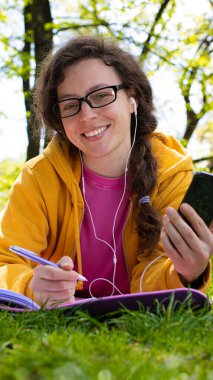 Neşeli, hayat dolu genç bir kadın en sevdiği müzik listesinin keyfini çıkarırken açık havada bir deftere mutlu bir şekilde yazıyor.