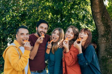 Gençler fotoğraf için poz verirken bir dilim pizzayla eğleniyorlar.