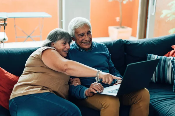 Gülümseyen Yaşlı Çift Evdeki Kanepede Oturmuş Dizüstü Bilgisayara Bakıyor Yaşlılar — Stok fotoğraf