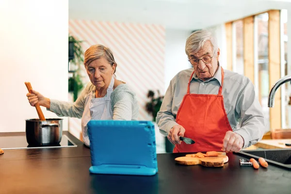senior couple using technology for cooking - elder people using on line blog tutorial recipes