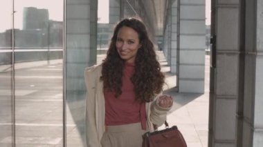 Çekici, uzun saçlı, zarif kıyafetli, kameraya gülümseyen esmer bir kadın. Yaşam tarzı, iş hayatı tarzı.