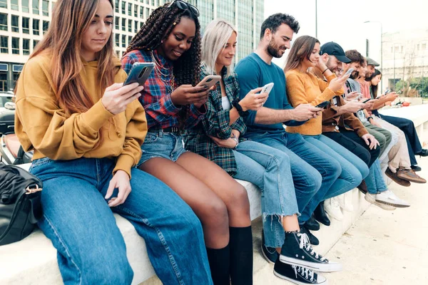 crowd of young people sitting in line outdoors surfing cyberspace with cell phone